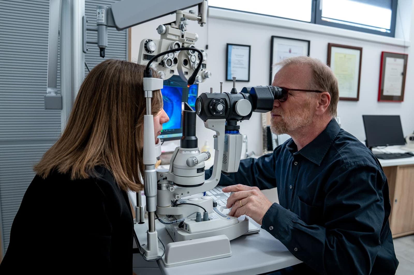 Augenoptiker untersucht das Auge einer Kundin an der Spaltlampe