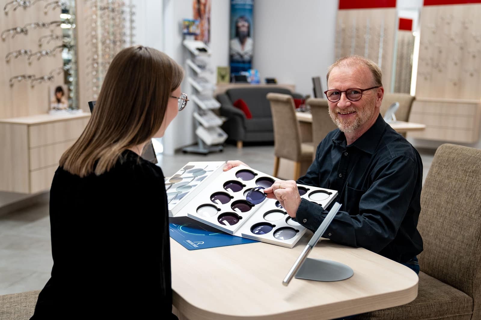 Augenoptiker zeigt einer Kundin Brillengläser aus einem Glasmusterkoffer