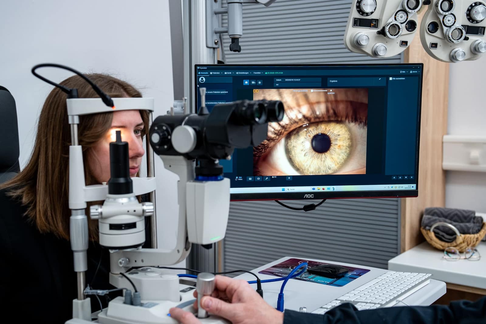 Kundin bei der Augenanalyse an der Spaltlampe, das Auge ist vergrößert auf dem Bildschirm zu sehen
