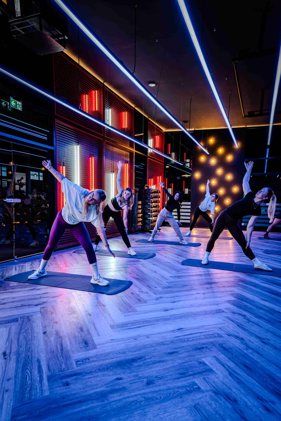 Group-Fitness-Kurs beim Stretching auf Matten im blau-roten Neonlicht des GymOne 24/7 Bitburg