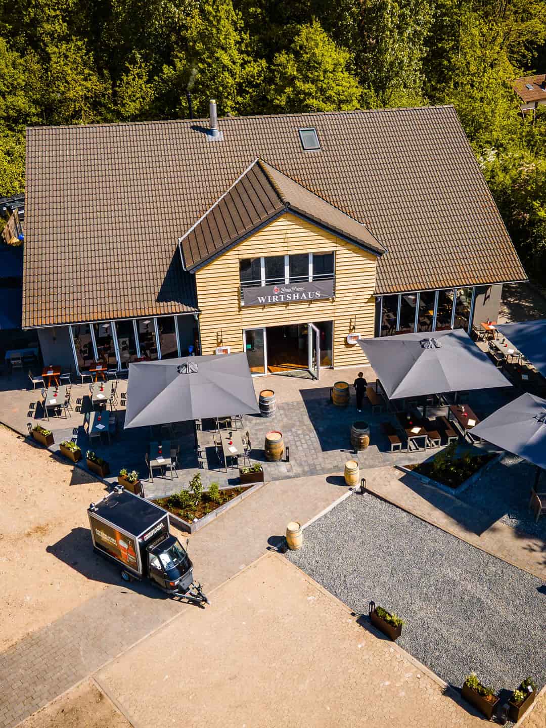 Luftaufnahme des König Pilsener Wirtshaus Moers mit Außenterrasse, Sonnenschirmen und Weinfässern