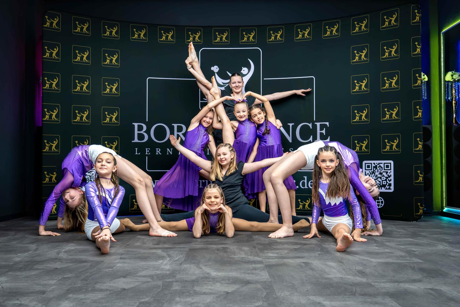 Kindertanzgruppe der Tanzschule Born to Dance in lila Kostümen posiert vor der Fotowand
