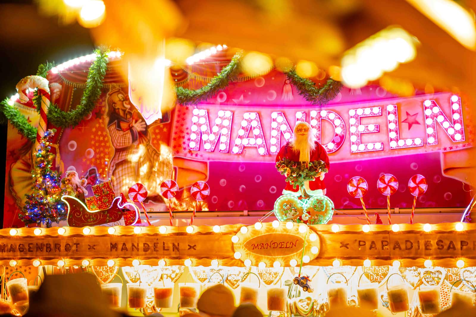 Hell beleuchteter Mandel- und Süßwarenstand auf einem Weihnachtsmarkt bei Nacht